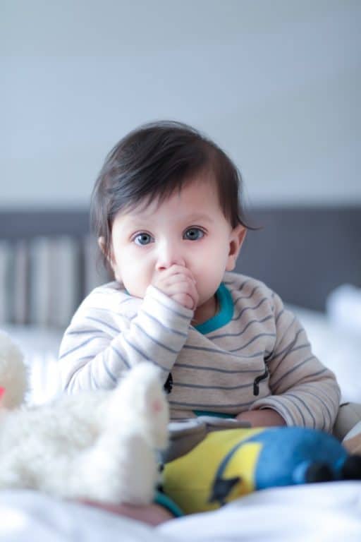 newborn hearing screening Baby sitting in a crib sucking his thumb