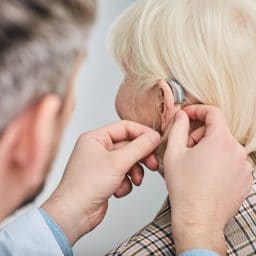 Audiologist fitting a hearing aid on an older female patient.
