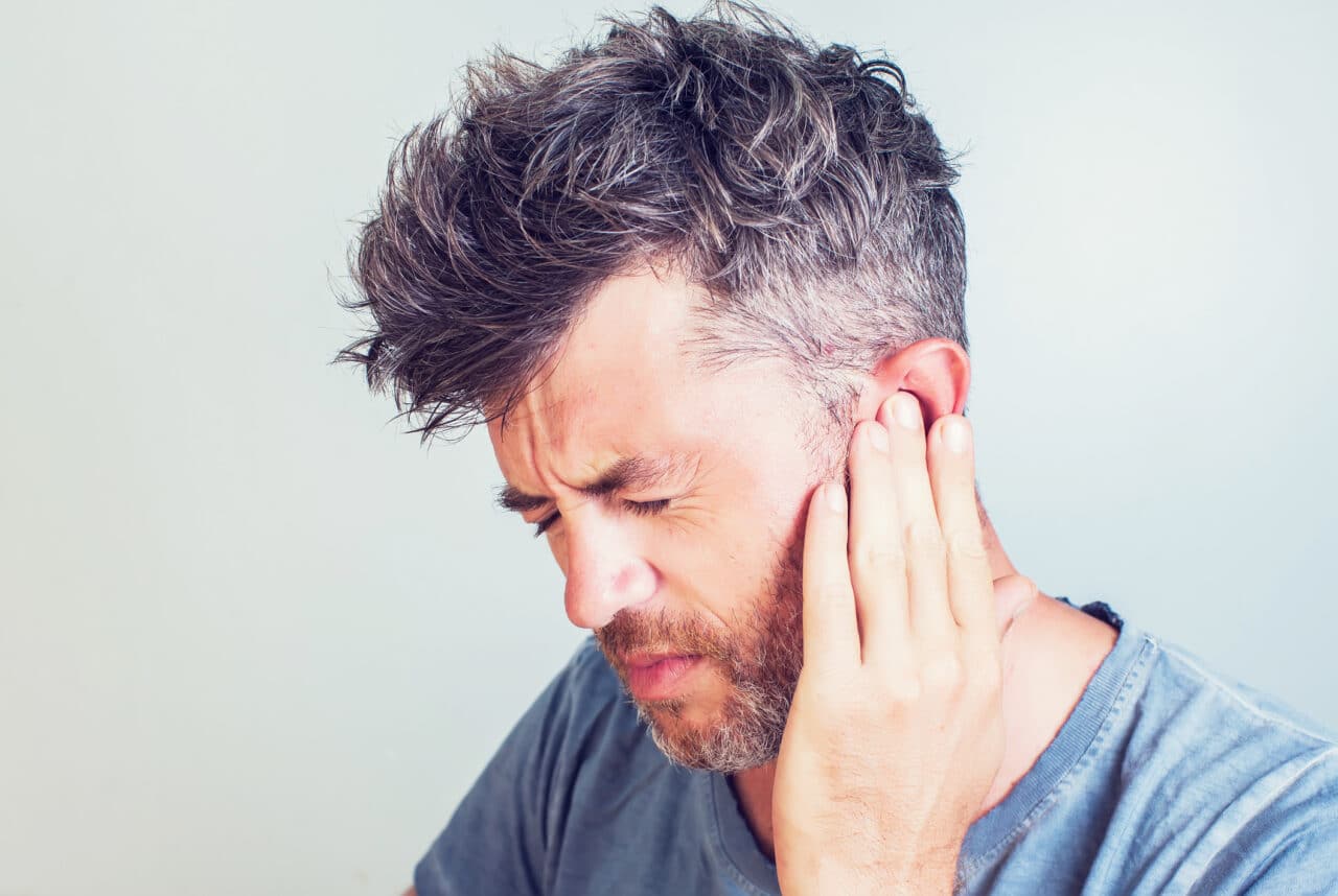Man with tinnitus holding his ear.