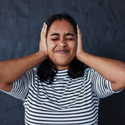 Woman holding her ears against a dark background