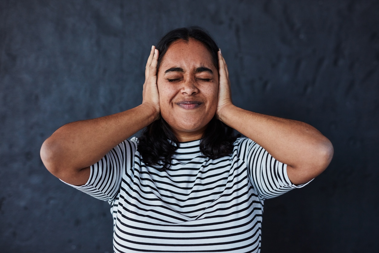 Woman holding her ears against a dark background