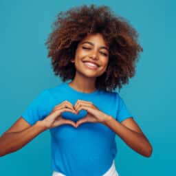 Smiling woman making a heart with her hands against a blue background.