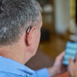 A man with a behind-the-ear hearing aid makes an appointment on his mobile phone.