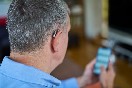 A man with a behind-the-ear hearing aid makes an appointment on his mobile phone.