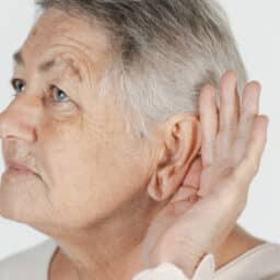 Portrait of an elderly woman holding her hand to her ear, representing hearing difficulties common in aging.