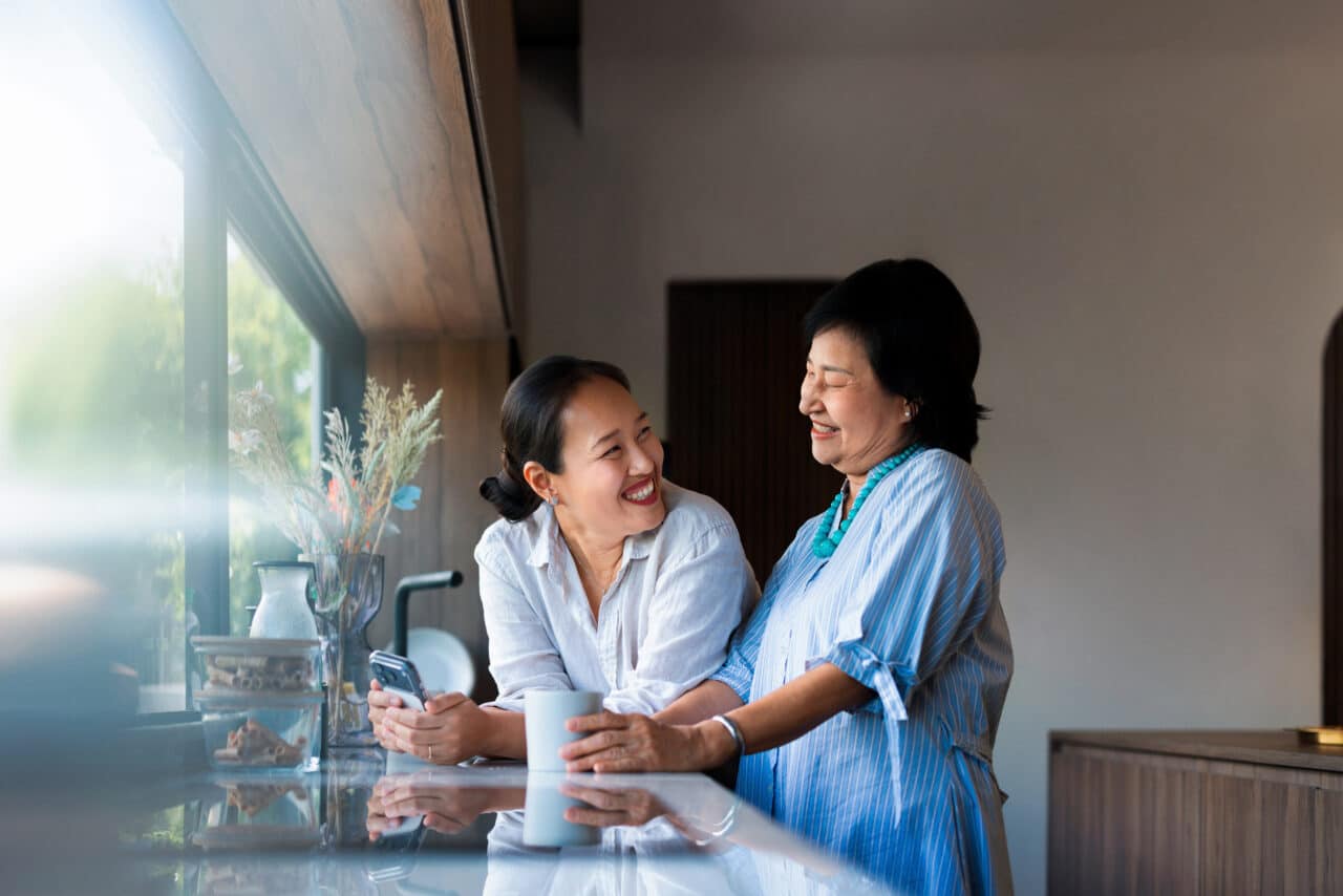 Woman and her adult daughter share a cup of coffee and laugh in the kitchen