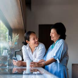 Woman and her adult daughter share a cup of coffee and laugh in the kitchen